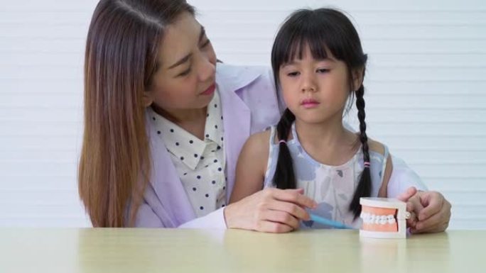 亚洲女牙医教可爱的小女孩用牙刷刷牙，口腔科医生告诉女孩儿童牙科诊所的口腔卫生，教育和预防蛀牙的概念。