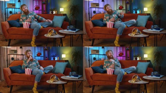男人坐在沙发上吃爆米花，在家看有趣的电视连续剧，在线体育游戏
