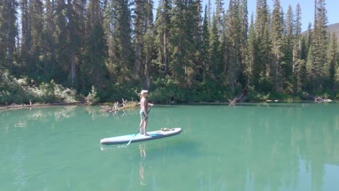 女人在站立的桨板上划桨，在山湖上