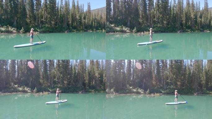 女人在站立的桨板上划桨，在山湖上