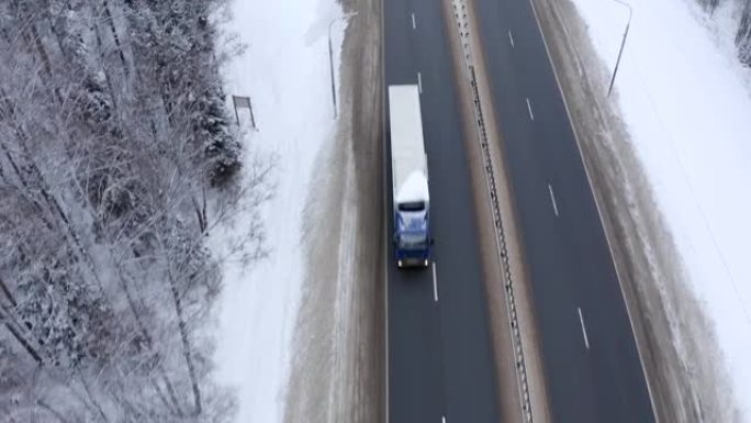 两辆卡车和一辆银色货车的屋顶沿着一条道路行驶，路边积雪和树木。