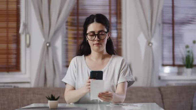 戴着眼镜的年轻漂亮白人妇女用智能手机扫描商店纸质收据上的QR码。会计与退税的概念