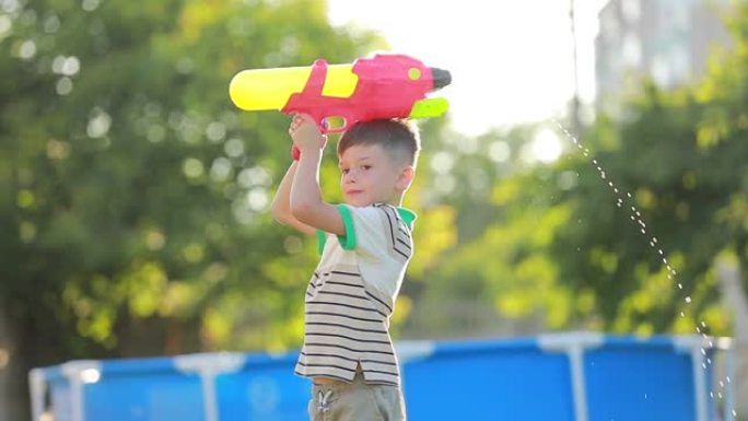在炎热的夏日，一个快乐的小男孩手里拿着水枪在后院的绿色草坪上慢动作的特写镜头。