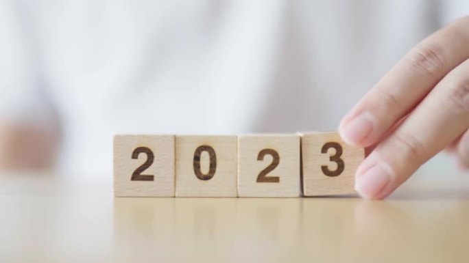 新的2022年变化2023年。用手把木方块和年号。新年决议，圣诞快乐