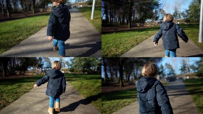 在阳光明媚的冬日里，小男孩穿着夹克和靴子在公园外面散步