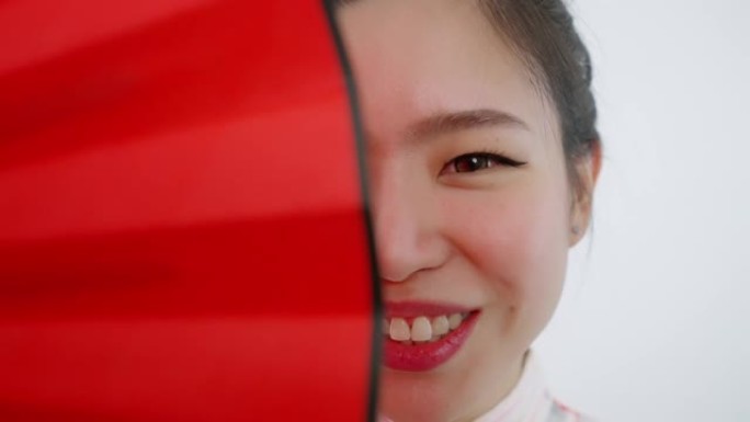 中国/亚洲美女脸特写春节红扇遮住右半张脸，微笑着看着镜头