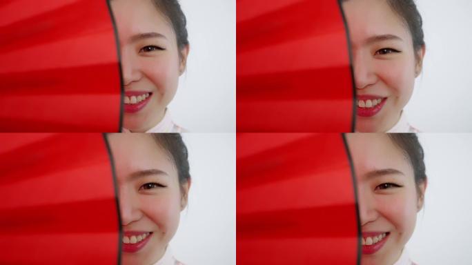 中国/亚洲美女脸特写春节红扇遮住右半张脸，微笑着看着镜头
