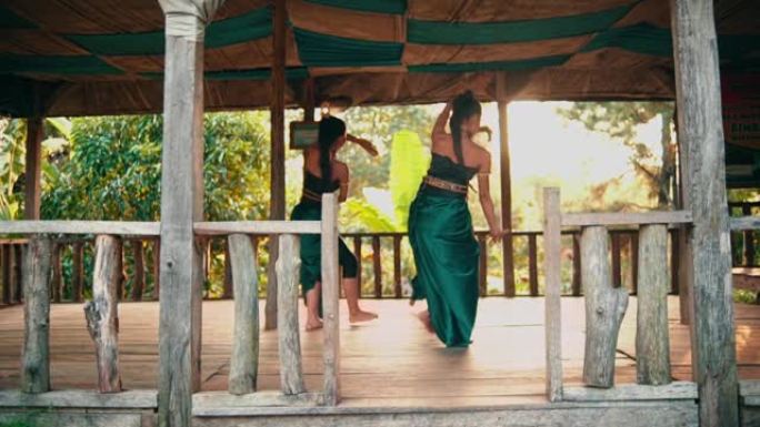 一群穿着绿色服装的亚洲女舞者在竹屋中一个悲伤的女人面前一起跳舞