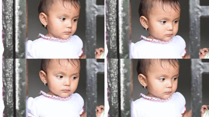 一个拉丁女婴看着窗外，一脸无聊。小女孩躲在窗栏后面。