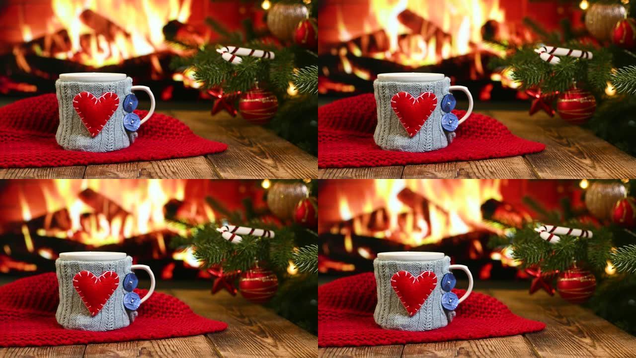 在燃烧的壁炉，红色格子和一棵圣诞树的背景下，在木制桌子上放着带有红色心形的蓝色针织罩子的热饮杯子