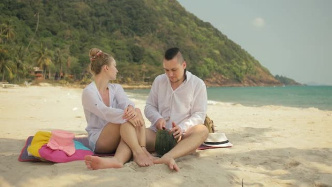 欢快的爱情夫妇在热带沙滩上拿着和吃西瓜片。浪漫的恋人两个人度过夏季周末