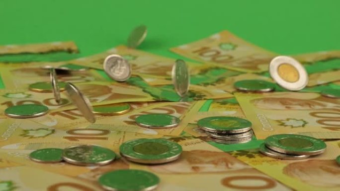 加拿大的钱。在100美元聚合物纸币上落下的加拿大硬币与罗伯特·博登的肖像。慢动作。在绿色背景上。