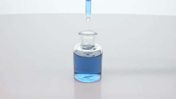 实验室滴管在灰色背景上将蓝色的变色油滴入瓶中