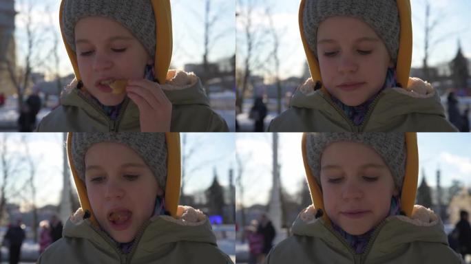 一个十几岁的孩子喜欢在外面吃饭。阳光明媚寒冷的冬日。这个女孩喜欢吃快餐土豆。热闹拥挤的地方