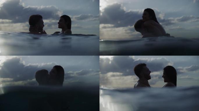 浪漫的异性恋夫妇在金色日落时在海里游泳。接吻