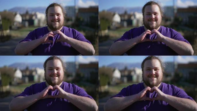 一个年轻的超重男子双手在外面做心脏标志。快乐胖乎乎的人做爱的象征表达关怀