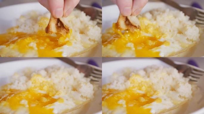 将软面包浸入煎鸡蛋的液态蛋黄中，然后食用。拿着一块面包的人的手指浸在蛋黄里吃。多莉镜头，特写