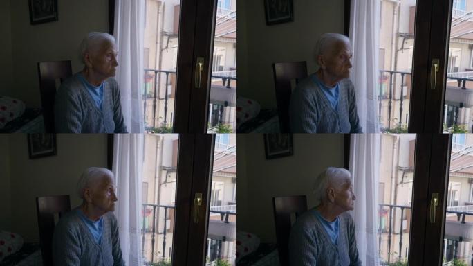 悲伤体贴的皱纹老妇人坐在阳台门的椅子上环顾四周，看着窗外。高级高加索女性退休人员在家室内思考的肖像。