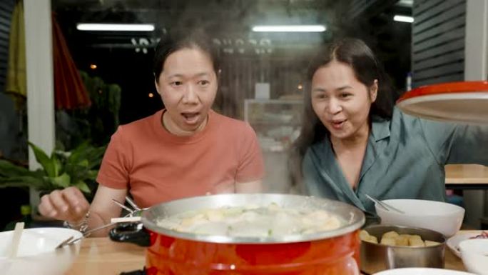 4k慢动作，一位穿着棕色和绿色衬衫的亚洲女性最好的朋友对即将煮熟并准备食用的红色锅中的sukiyak