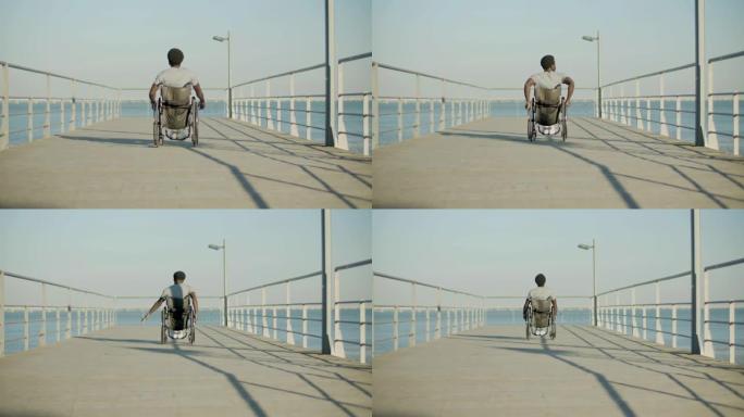 黑人在海滨骑轮椅的后视图镜头。