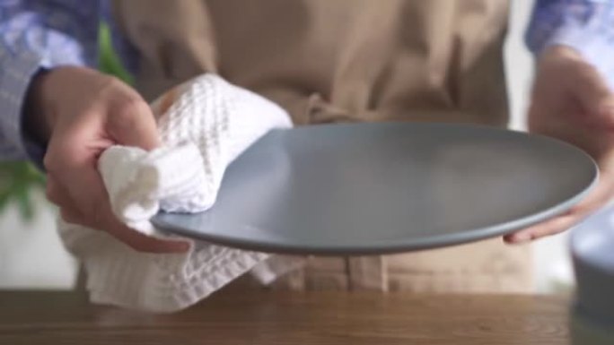 女主人用白色茶巾擦拭一个大的灰色盘子。房子周围的日常概念