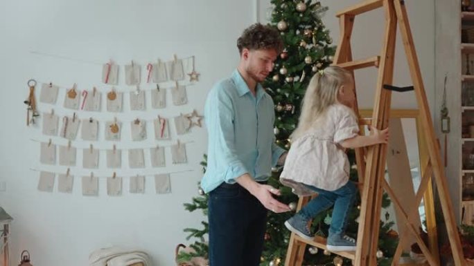 积极的父亲帮助女儿在圣诞节在家爬梯子