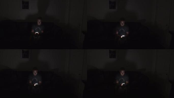 一名男性在黑暗中看着坐在沙发上的智能手机