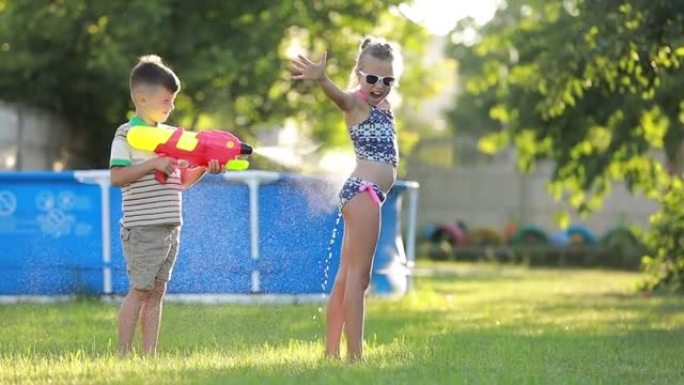 小男孩正在给她姐姐泼水。快乐快乐的孩子在花园里玩水枪的慢动作视频。