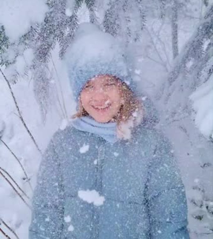 降雪。一个可爱的女孩，穿着蓝色外套，在白雪覆盖的云杉下。