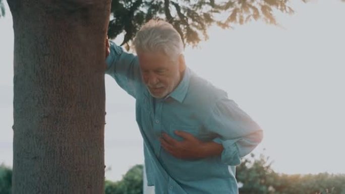 头部特写肖像生病的老人在公园摸他的胸部感觉不好。疲惫的成熟雄性在树旁边休息。