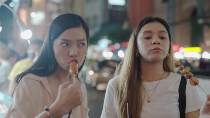 两名女性游客在著名的唐人街的小吃摊前品尝烤制的便餐并讨论口味。