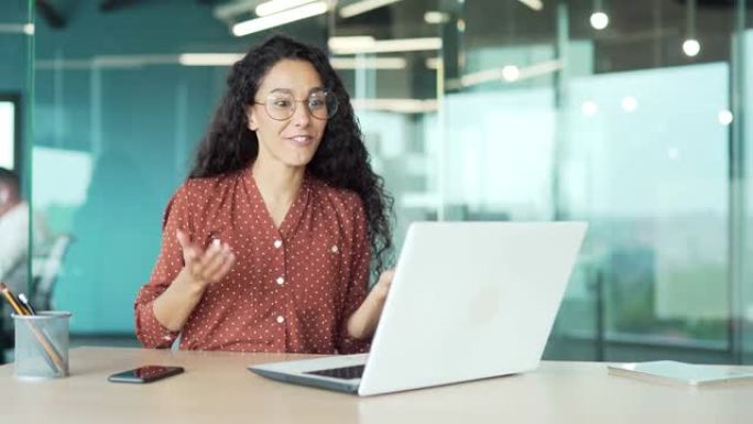 快乐的年轻美丽的商业女性卷发和眼镜西班牙裔积极的员工在视频通话中使用笔记本电脑进行远程通信