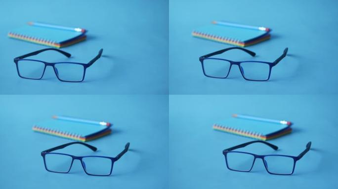 记事本、眼镜和蓝色背景上的铅笔