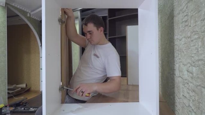 年轻人，一个专业的家具组装商，安装厨柜门。