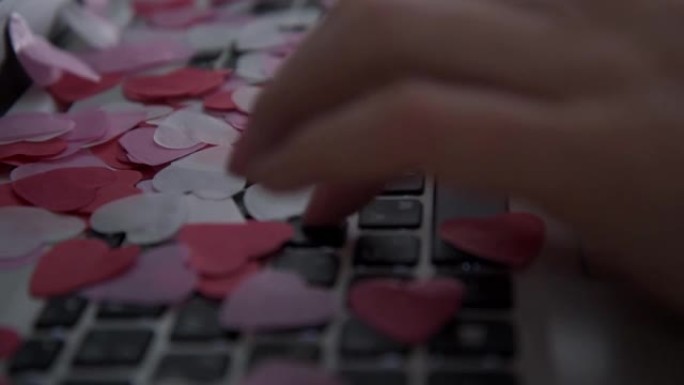 妇女的手在笔记本电脑键盘上打字。心形的五彩纸屑开始从上面倾泻。情人节祝贺的概念。情书的概念。电子形式