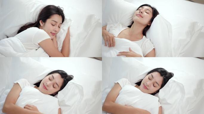 美丽的亚洲女人躺在床上。年轻女子在柔软的白色亚麻枕头上舒适舒适的新鲜床上睡得很好。早上在卧室里。健康