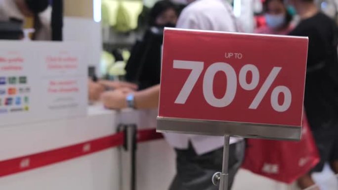 红色标志与70% 折扣，以吸引顾客。在blur的背景中，结帐时无法识别的顾客渴望在商店中以便宜的价格