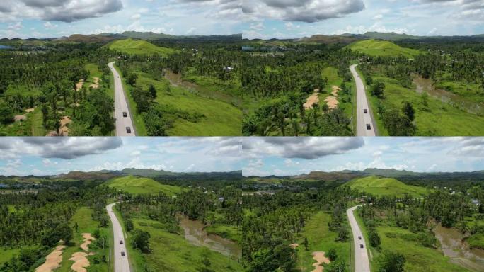 令人惊叹的森林和丘陵景观的电影鸟瞰图。一个绿色的热带岛屿，有许多常绿乔木。黑色汽车行驶的道路绕过一座