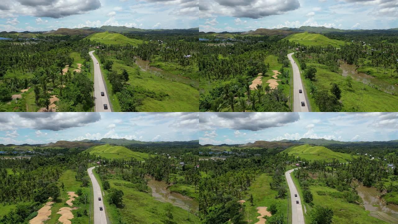 令人惊叹的森林和丘陵景观的电影鸟瞰图。一个绿色的热带岛屿，有许多常绿乔木。黑色汽车行驶的道路绕过一座