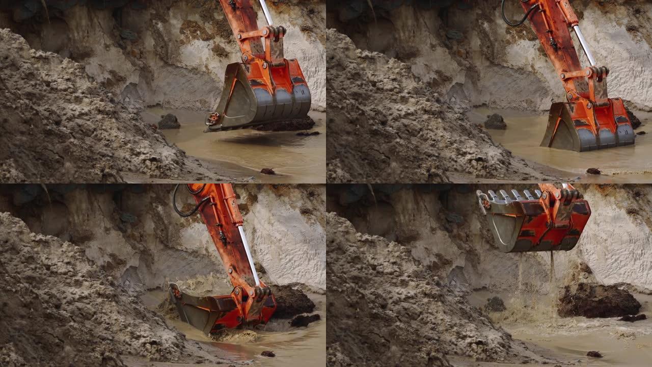 大型挖掘机铲斗的特写镜头从施工现场的一个坑中挖出泥土和水