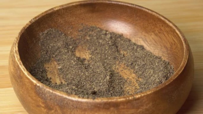 勺子从木碗中拾取磨碎的黑胡椒香料，然后在木板上旋转。用勺子干调味料。用于烹饪的香料和草药，胡椒粉