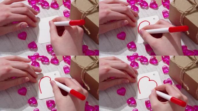用红色毡尖笔手绘，在一张带有心形和礼物的桌子上的白纸上标记心形。情人节礼物的自制标签。爱与和平的主题