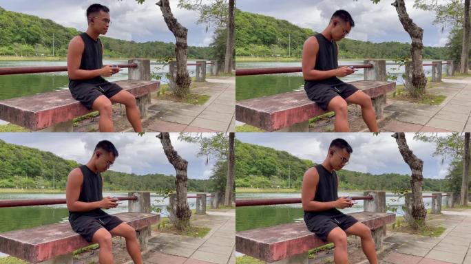 坐在湖边公园长椅上的带无线耳塞和手机的菲律宾年轻人