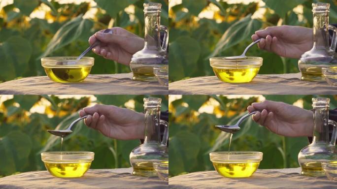 女人的手在透明的碗里用勺子舀起葵花籽油，涓涓细流。葵花籽油