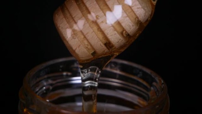 从黑色背景上的木制蜜勺中流出蜂蜜