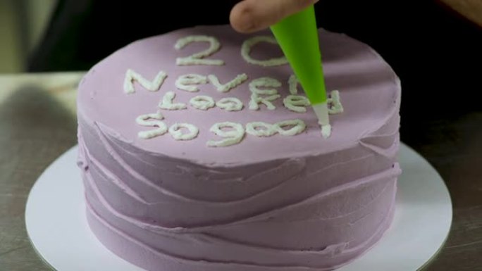 糕点师装饰紫色磨砂生日蛋糕，上面印有文字，撒上，珍珠和蝴蝶。