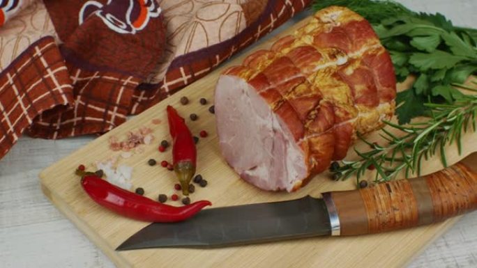 传统火腿放在木砧板上，配有雕刻刀、五颜六色的多香果、红辣椒、欧芹、莳萝和罗勒。从猪肉中吃出美味肉食小