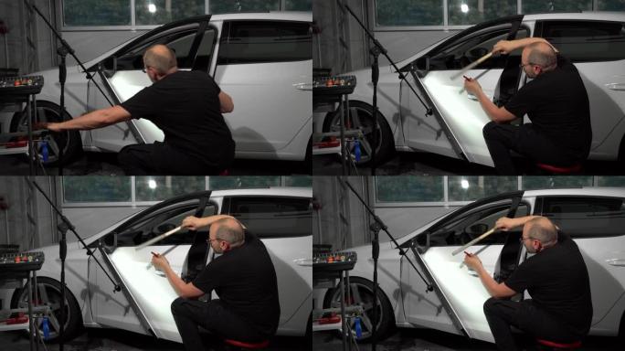 汽车修理厂修理车门表面凹痕的视频过程。技术人员正在使用工具进行无油漆凹痕修复。事故后损坏的车身。