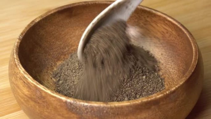 勺子将磨碎的黑胡椒放在木板上的木碗中并旋转。用勺子干调味料。用于烹饪的香料和草药，胡椒粉