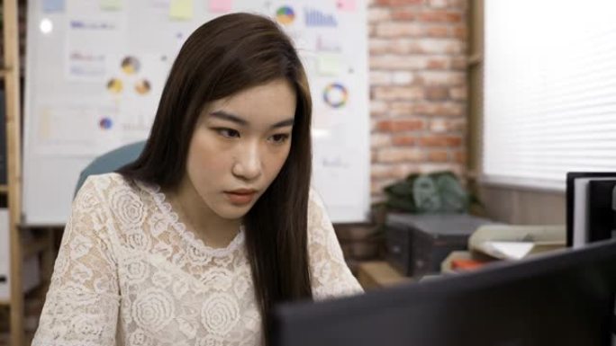 肩膀射击不舒服的亚洲女商人坐在电脑后面揉眼睛，努力眨眼，试图在办公室里看清楚。